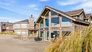 Una casa moderna frente a la playa con ventanas amplias, un balcón y un camino de entrada de arena.