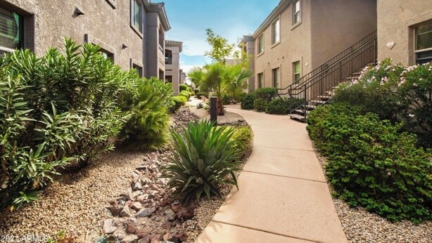 Un edificio residencial con un sendero pavimentado, rodeado de jardines cuidados y una escalera que conduce a la entrada.