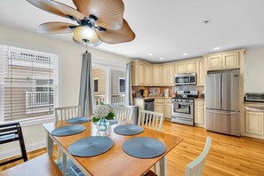 A modern kitchen with a dining area, wooden flooring, and a ceiling fan. - Hot Tub + Pool | Cozy Stay | Washer/Dryer | Coffee (Seaside Heights)