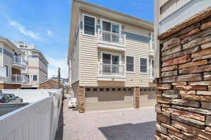 A multi-story residential building with a garage, a balcony, and a stone accent wall. - Hot Tub + Pool | Cozy Stay | Washer/Dryer | Coffee (Seaside Heights)