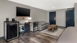 A compact hotel room with a bed, a desk with a computer, a small refrigerator, a sofa, and a TV mounted on the wall. - Red Lion Inn & Suites Kansas City (Kansas City)