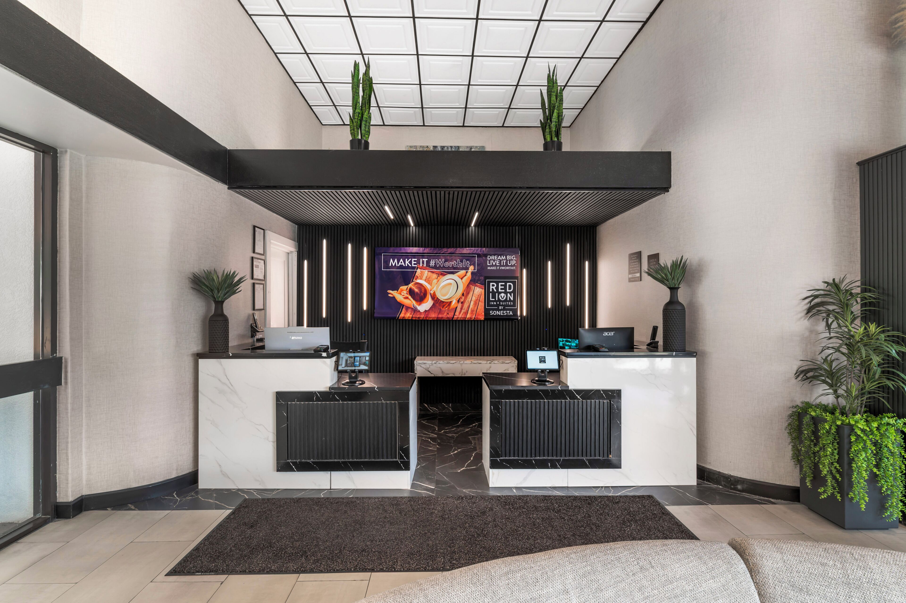 Un espace d’accueil d’hôtel au design moderne, comprenant un grand écran numérique, des comptoirs d’accueil et des plantes en pot.