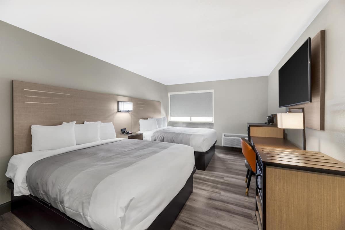 A hotel room with two beds, a desk, a TV, and a window.