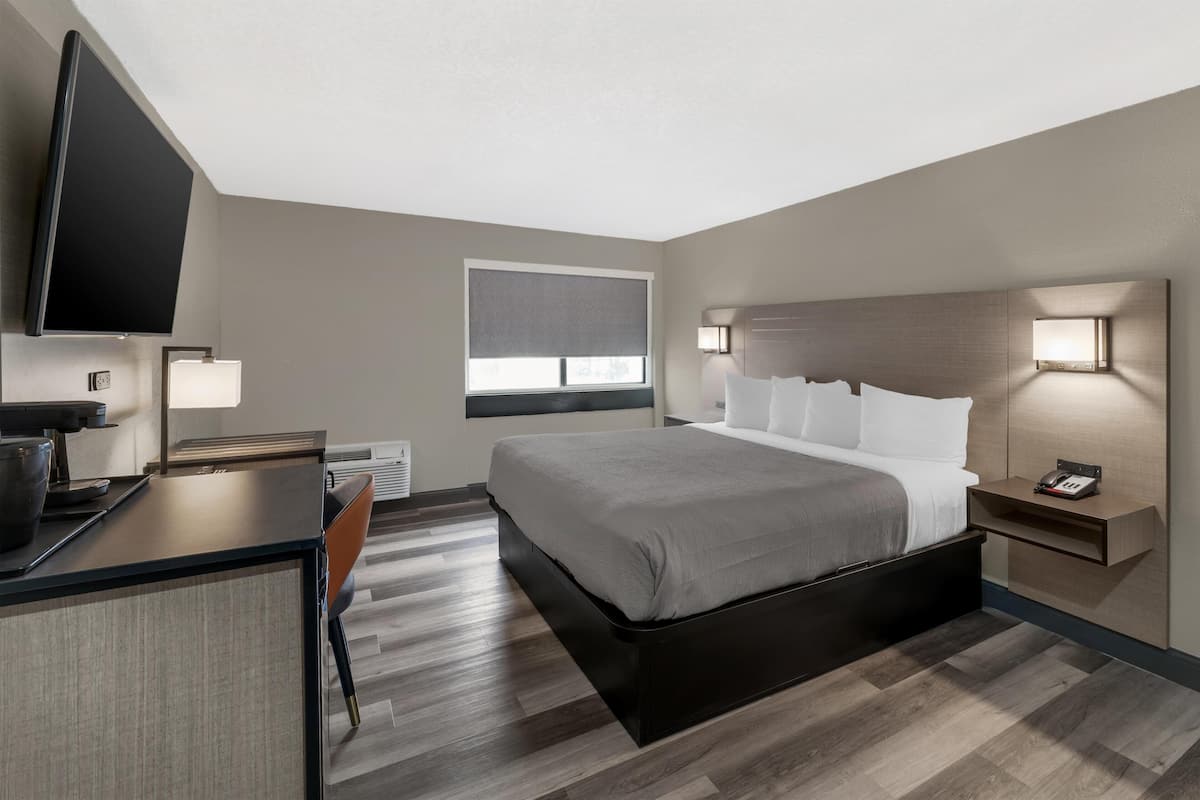 A modern hotel room with a bed, desk, chair, TV, window, and bedside lamps.