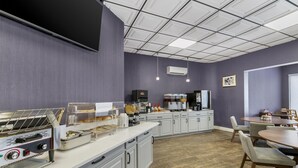 A modern kitchen with a flat-screen TV, coffee machines, and a buffet setup. - Red Lion Inn & Suites Kansas City (Kansas City)
