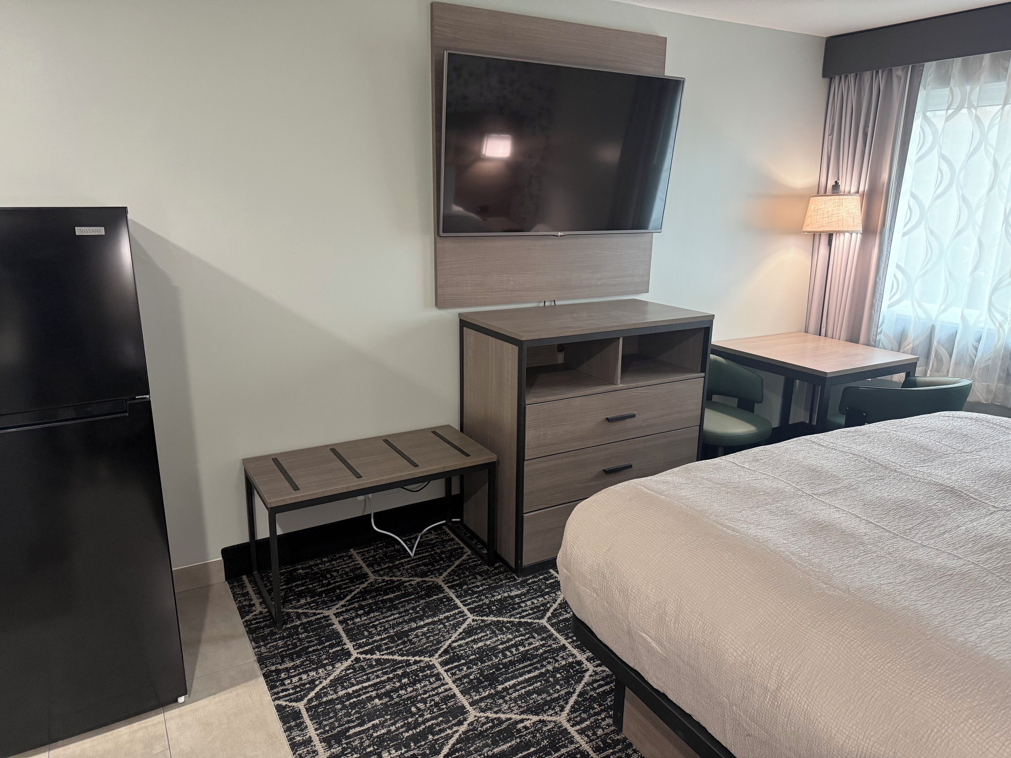 A hotel room with a bed, a TV mounted on the wall, a desk, and a chair.