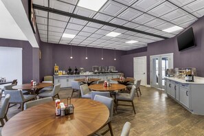 Un comedor moderno con mesas redondas, sillas y una cocina al fondo.