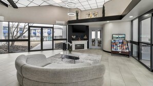 A modern lobby with a sofa, a fireplace, a TV, and a magazine rack. - Red Lion Inn & Suites Kansas City (Kansas City)