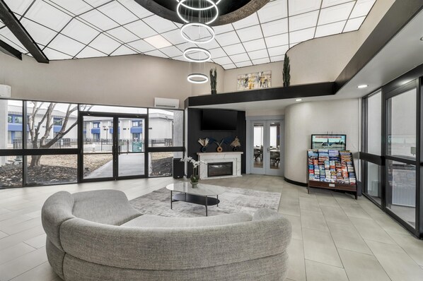A modern lobby with a sofa, a fireplace, a TV, and a magazine rack. - Red Lion Inn & Suites Kansas City (Kansas City)