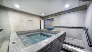 Ένα σύγχρονο μπάνιο με έναν τοίχο επενδυμένο με πέτρινα πλακάκια, μια μπανιέρα υδρομασάζ με γυάλινο περίβλημα και μια μαύρη μεταλλική μπάρα στήριξης.