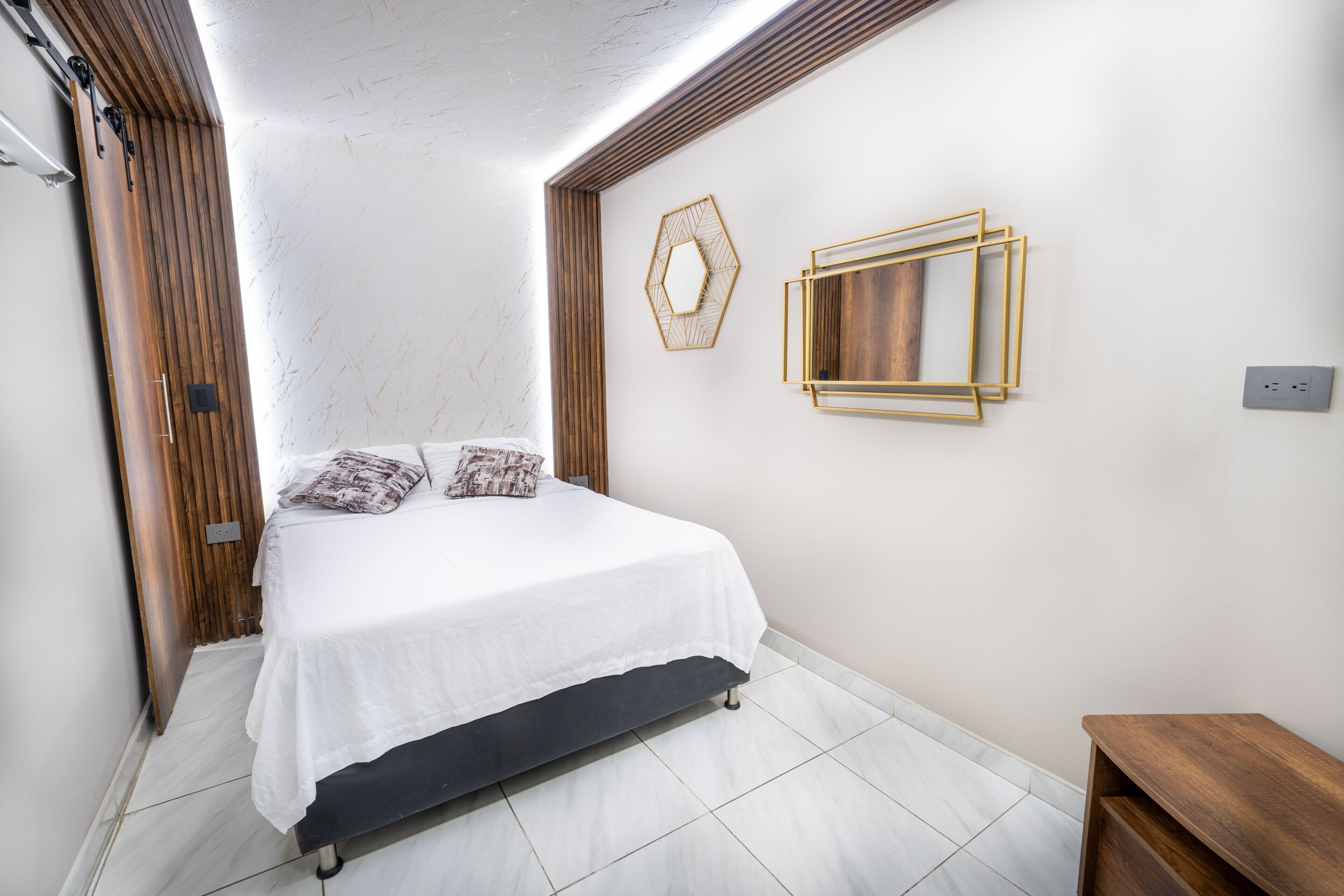A bedroom with a bed, wooden paneling, a geometric wall decoration, and a small wooden bench.