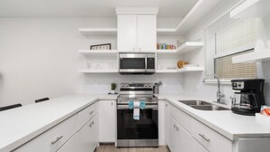 Una cucina moderna con mobili bianchi, forno in acciaio inossidabile, microonde e macchina per il caffè.