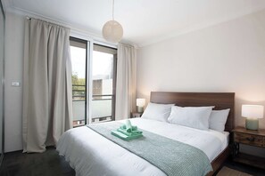 A hotel room with a bed, a nightstand, a lamp, and a view through a large window. - Urban Oasis 2BR with Huge Deck & Secure Parking (Potts Point)