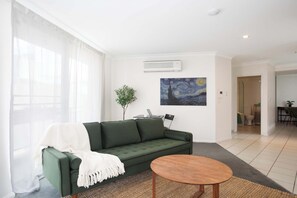 Ein modernes Wohnzimmer mit einem grünen Sofa, einem runden Holztisch, einem Bild an der Wand und einer Pflanze.