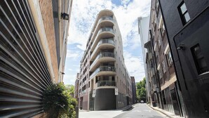 Un edificio de varios pisos con balcones, una entrada protegida por un portón y un cielo despejado.