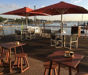 A waterfront patio with tables and chairs, red umbrellas, and a view of the water. - Urban Oasis 2BR with Huge Deck & Secure Parking (Potts Point)