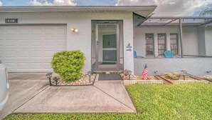 Uma casa residencial com garagem, porta da frente, um pequeno jardim com arbusto e uma bandeira americana.