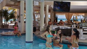 Un espace piscine doté d’un bar et de coins salon, entouré de palmiers et offrant une vue sur l’océan.