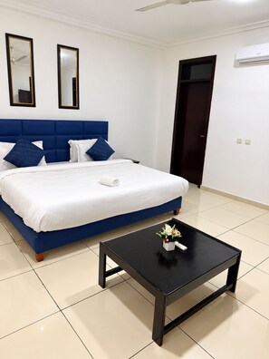 Habitació d'hotel amb un llit, dos miralls, un ventilador de sostre, aire condicionat i una taula petita amb un vas.