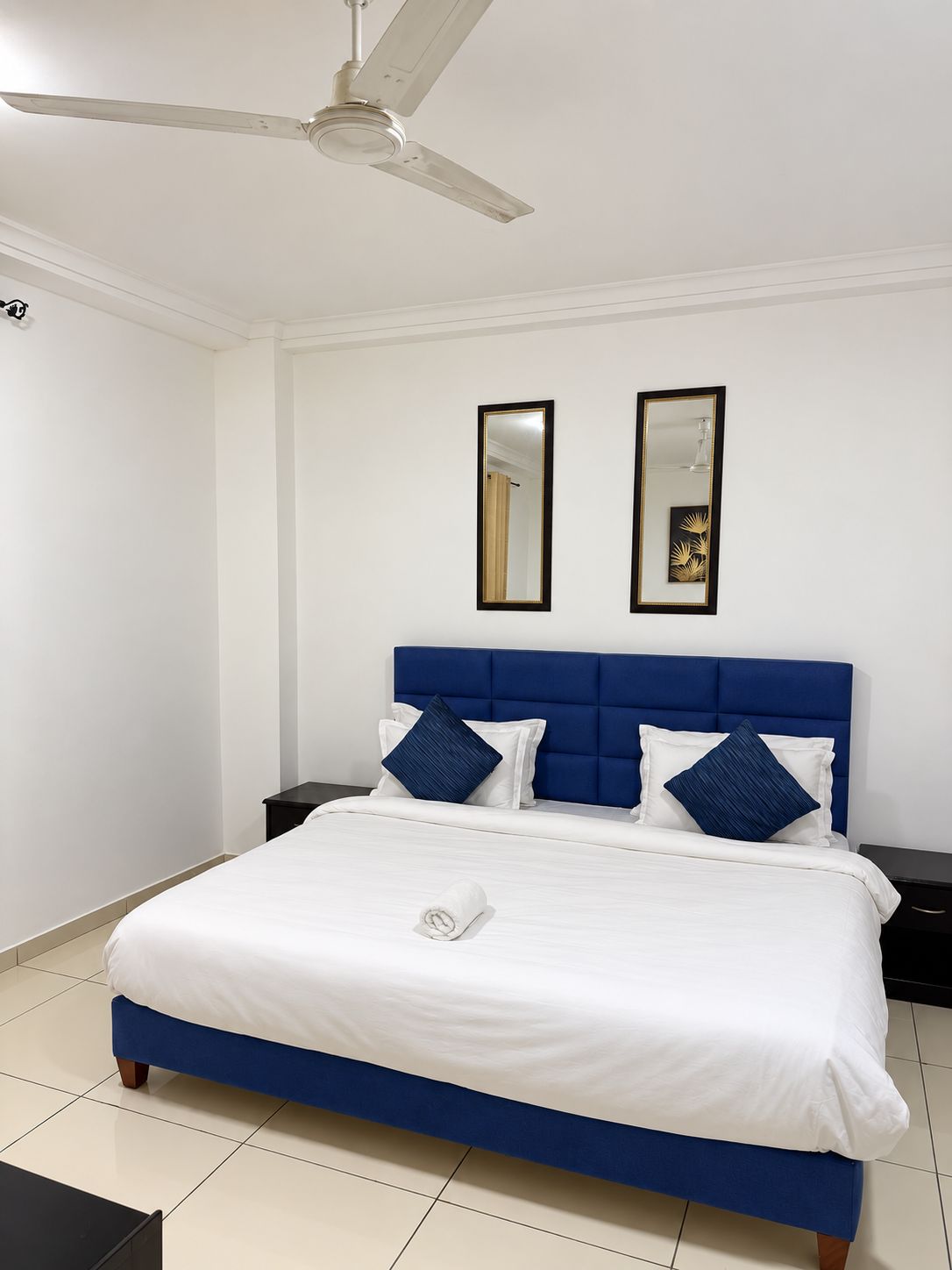 Une chambre d’hôtel comprenant un lit, deux tables de chevet, un ventilateur de plafond et deux miroirs fixés au mur.