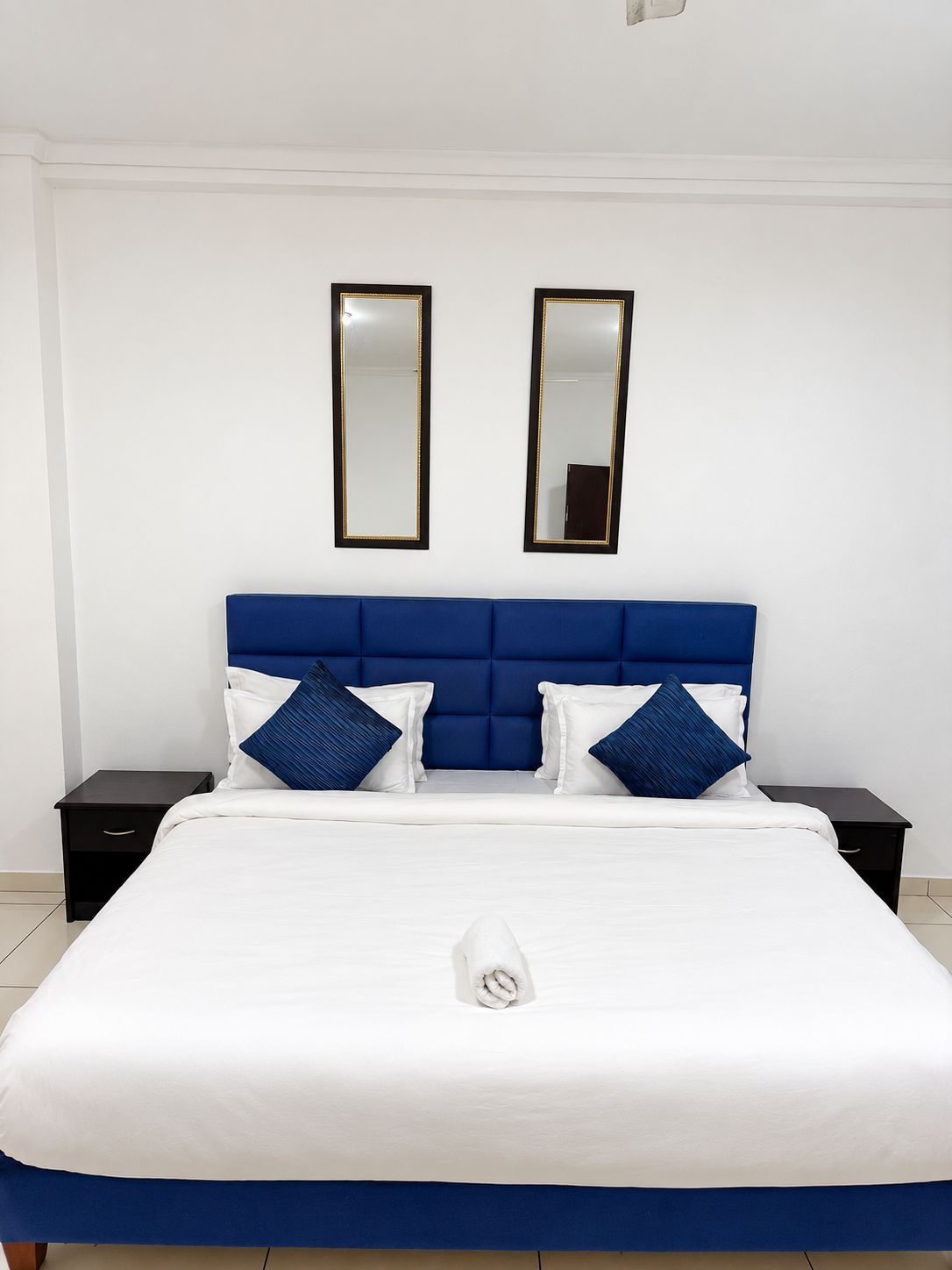 Une chambre d’hôtel avec un grand lit, deux tables de chevet et deux miroirs muraux.
