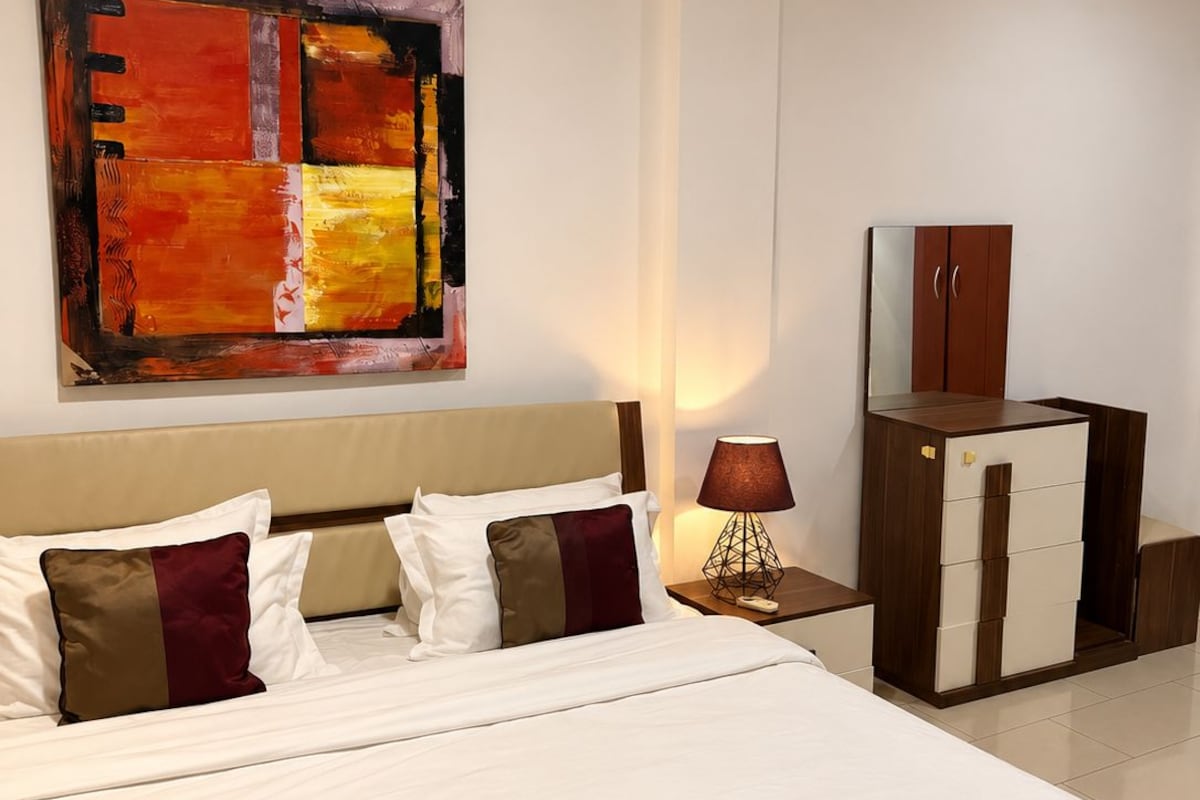 Una habitación de hotel con una cama grande, una mesita de noche, una lámpara, un armario y un cuadro en la pared.