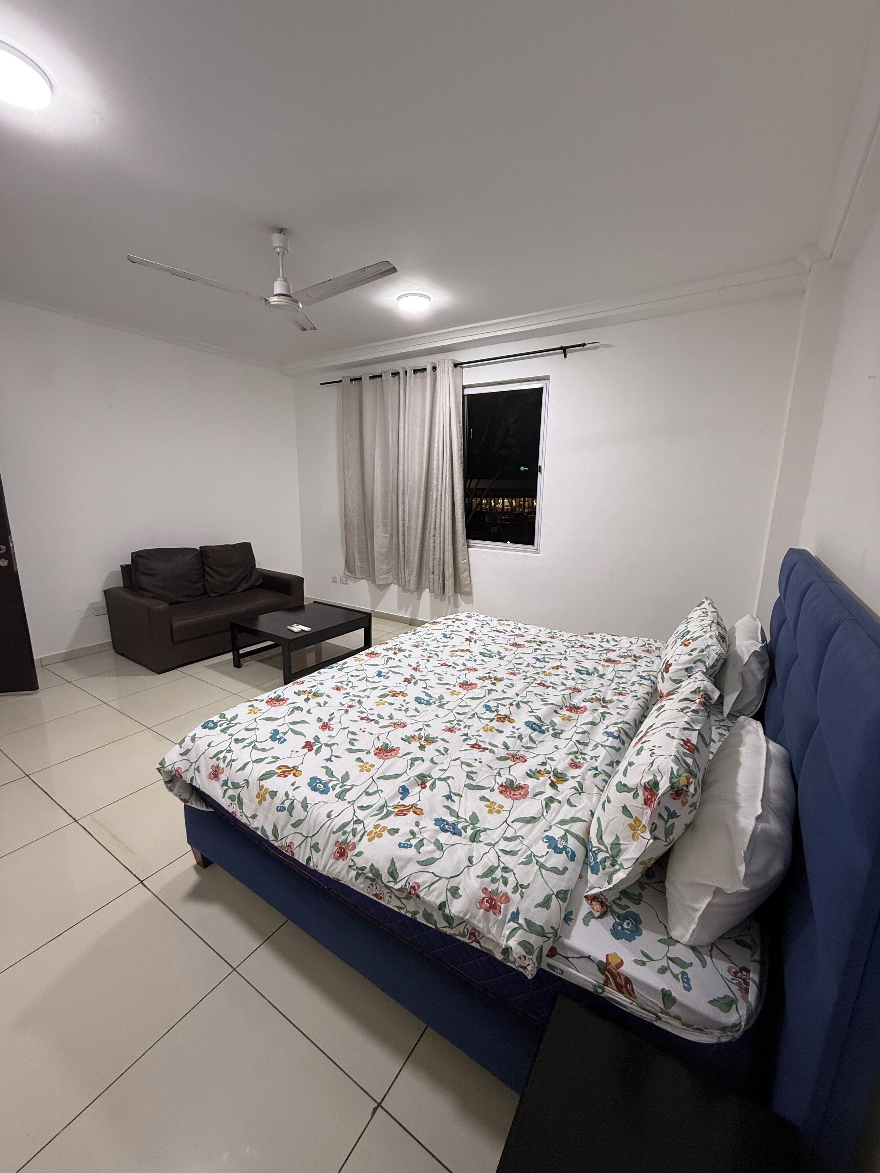 A bedroom with a bed, a sofa, a coffee table, a ceiling fan, and a window with curtains.