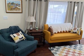A living room with a blue armchair, a yellow sofa, a lamp, and a painting on the wall. - Private bungalow close to LMU, ARH, Cumberland Gap (Middlesboro)