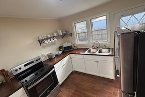 A kitchen with white cabinets, a stainless steel refrigerator, a microwave, and a stove. There are two windows providing natural light. - Private bungalow close to LMU, ARH, Cumberland Gap (Middlesboro)