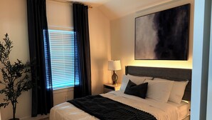 Ein Hotelzimmer mit einem großen Bett, einem Nachttisch mit Lampe, einer Topfpflanze und einem Bild an der Wand.
