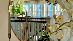Ein Zimmer mit Holzwertkasten, einem Blumentopf und einem Spiegel, der einen Balkon mit Geländer und Fenstern reflektiert.