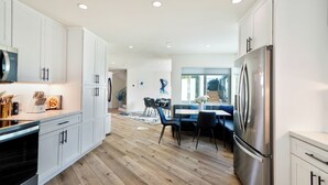 A modern kitchen with white cabinets, a stainless steel refrigerator, and a wooden floor.