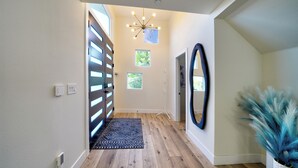 A modern hallway with a wooden floor, a patterned rug, a ceiling light fixture, and a potted plant.
