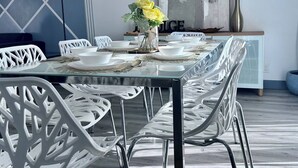 Un coin repas avec une table en verre, des chaises blanches et un vase rempli de fleurs jaunes.