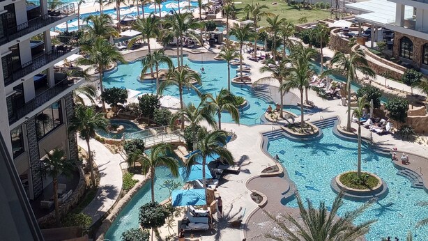 Un resort con varias piscinas, palmeras y vista al mar.