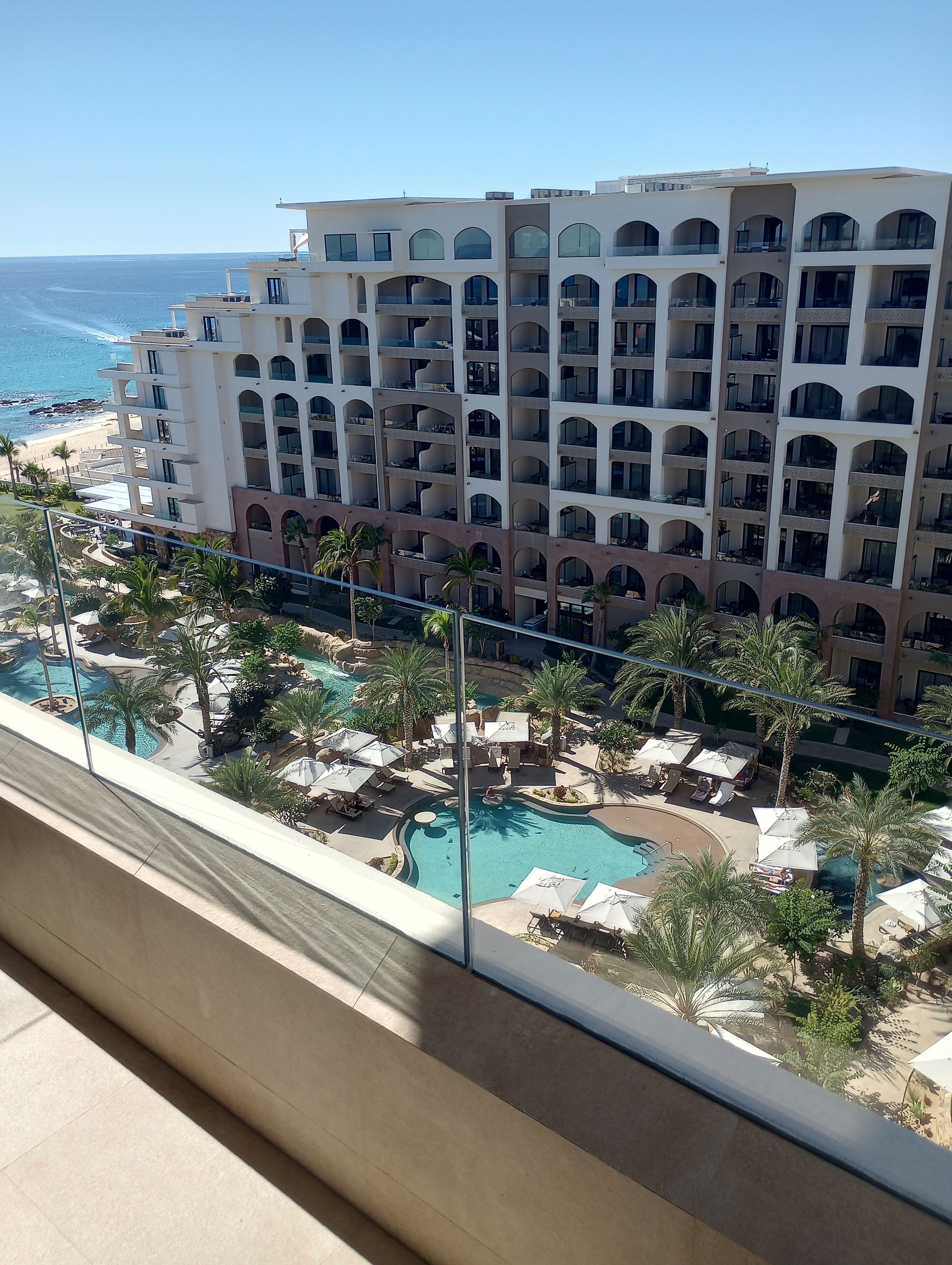 Un hôtel doté de nombreux balcons donnant sur une plage et d’un espace piscine avec des chaises longues et des parasols.