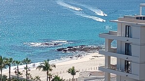Un hotel frente a la playa con piscina, palmeras y vista al océano.