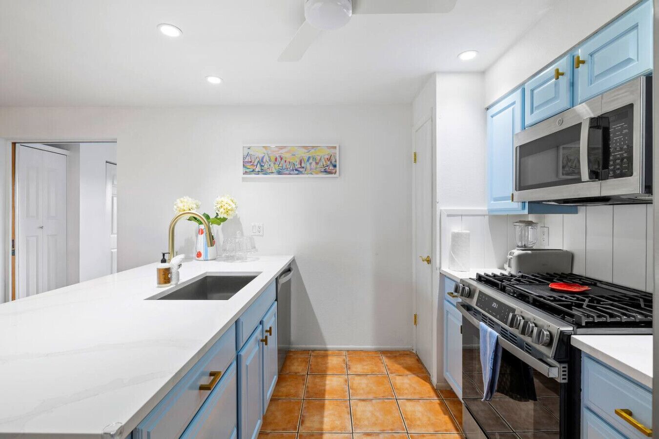 A modern kitchen with white cabinets, a large island, a stove, and a microwave.