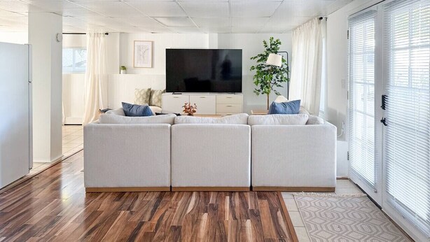 Una sala de estar moderna con un sofá modular, un televisor de pantalla plana y un ventanal con persianas.
