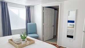 Habitación de hotel con una cama grande, un pequeño espacio de descanso, una puerta que conduce a otra habitación y un espejo en la pared.