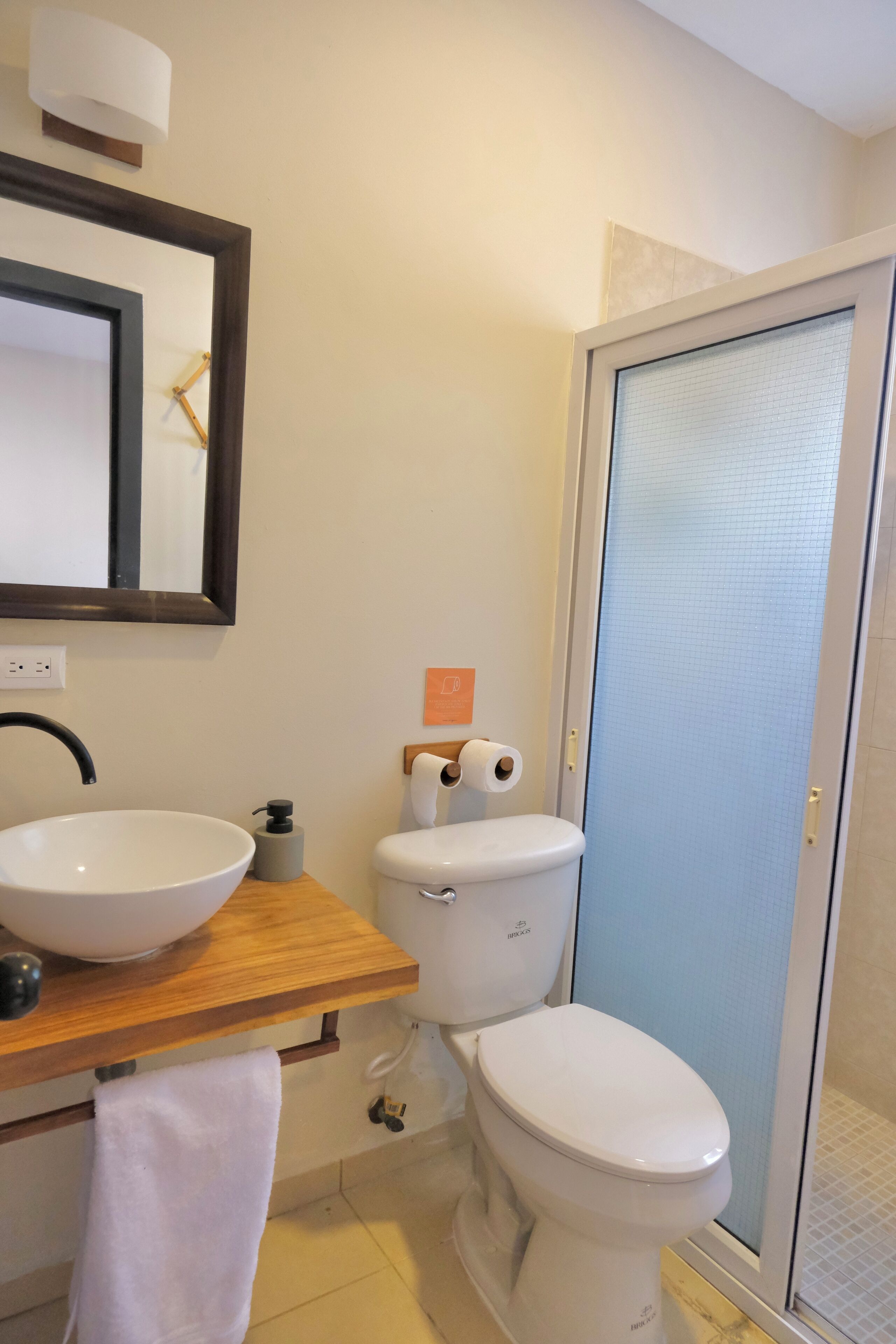 Un baño con tocador de madera, un lavabo blanco, un inodoro y una cabina de ducha de vidrio.