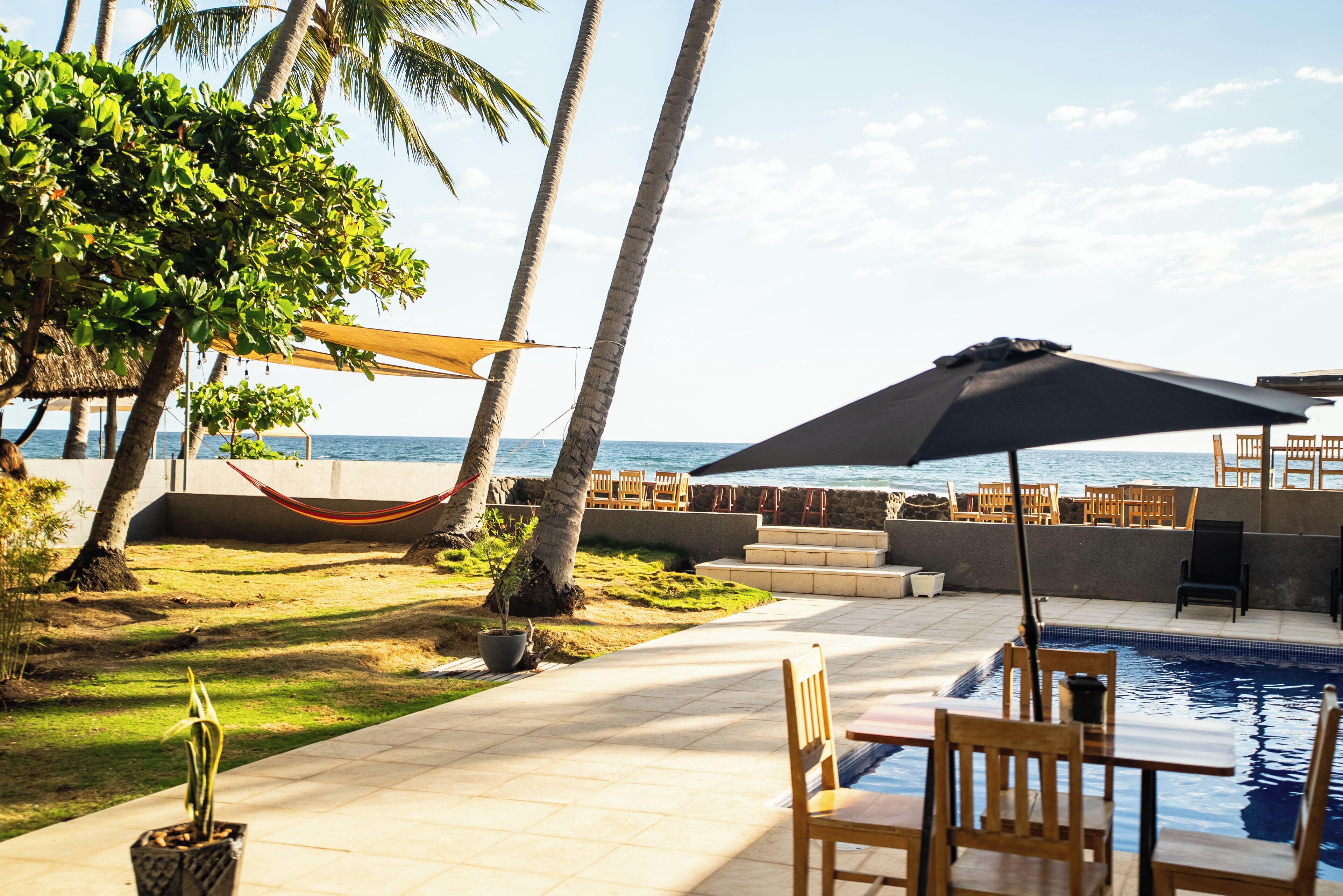 A poolside area with a table and chairs, a hammock, and a view of the ocean.