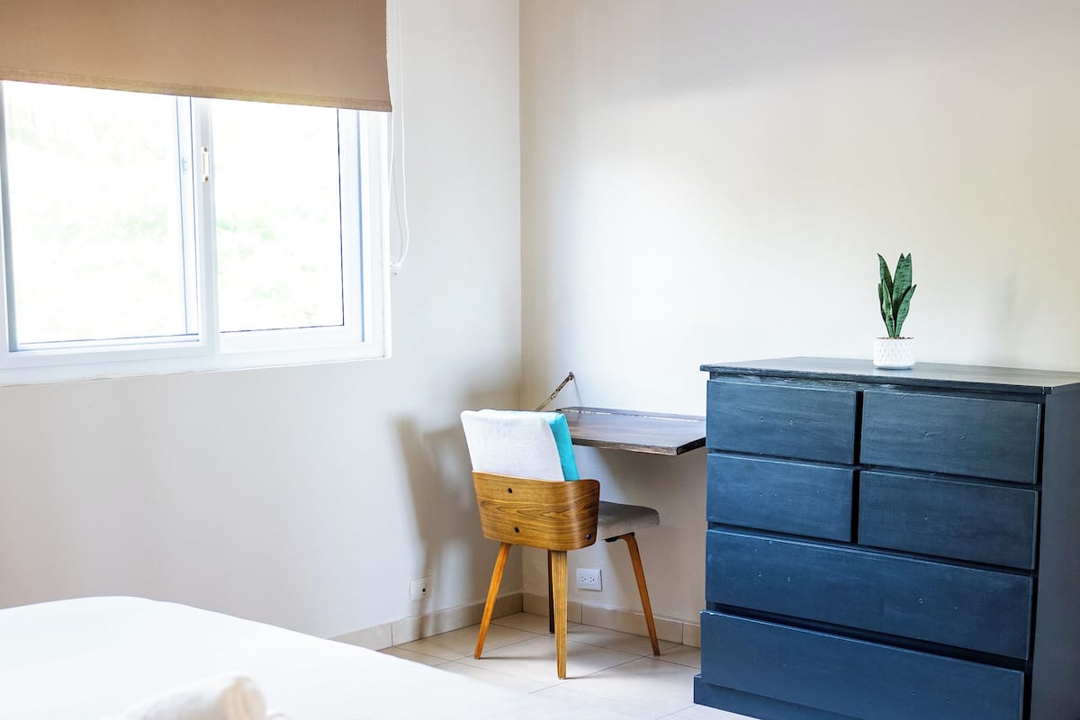 A bedroom with a bed, a desk, a dresser, and an air conditioning unit.