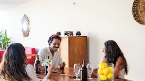 Un tavolo da pranzo in legno con un contenitore di vetro pieno di limoni, una bottiglia e bicchieri da vino.