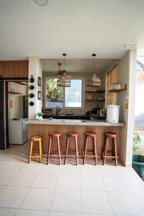 Cocina moderna con una isla central, taburetes de bar, luces colgantes y vistas al exterior.
