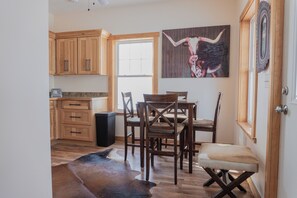 A dining area with wooden chairs and a table, a cowhide rug, and a painting of a cow on the wall. - Charming Cabin Hideaway, Peaceful Woodland Escape (Williamston)