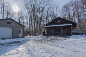 A snow-covered rural area with a wooden building and a metal shed. - Charming Cabin Hideaway, Peaceful Woodland Escape (Williamston)