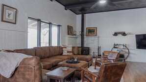 A cozy living room with a brown leather sofa, a wooden coffee table, and a fireplace. - Charming Cabin Hideaway, Peaceful Woodland Escape (Williamston)
