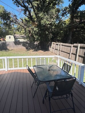 A covered outdoor deck with a table and chairs, surrounded by a white fence and trees. - Quaint 3-bedroom house with AC in welcoming Wichita (Wichita)