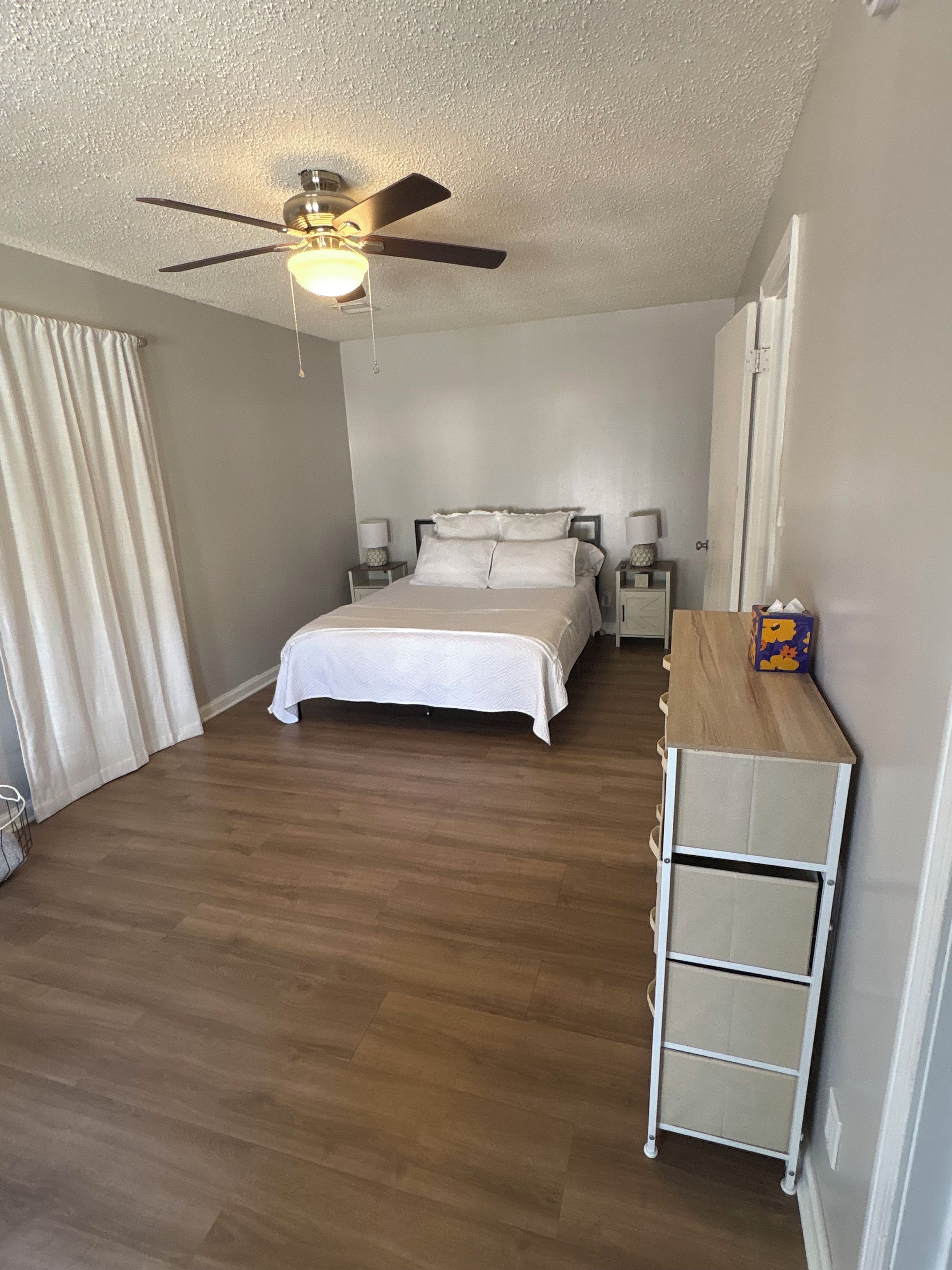 A bedroom with a bed, a ceiling fan, bedside lamps, a nightstand, and a wooden dresser.